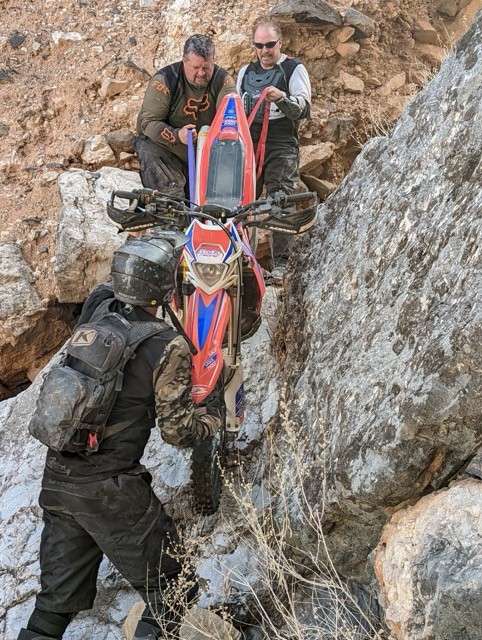 Riders helping lift a bike over rocky terrain